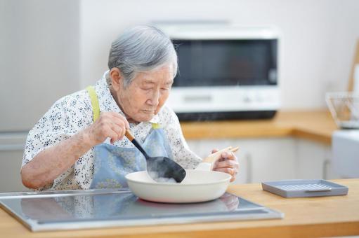 真剣な顔でフライパンを見つめる高齢女性 女性,料理,フライパンの写真素材