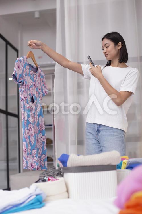ワンピースを持ってスマホで撮影する女性（縦）1 女性,主婦,母の写真素材