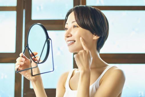 家で鏡を見てスキンケアする女性 家で鏡を見てスキンケアする女性 スキンケア,お手入れ,女性の写真素材