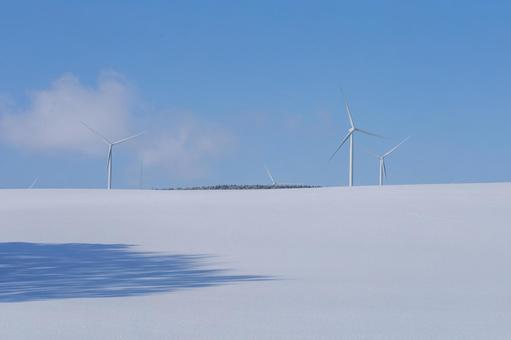 雪が積もった丘と風力タービン 雪が積もった丘と風力タービンの写真