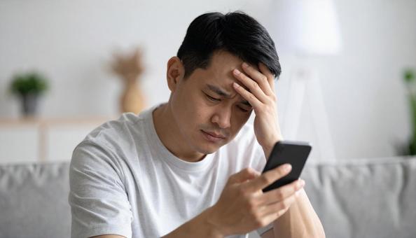 スマホの通知を見て悩むアジア人男性の表情 スマホの通知を見て悩むアジア人男性の表情の写真