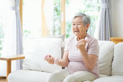 ソファでダンベルを持つ高齢女性 女性,ダンベル,持つの写真素材