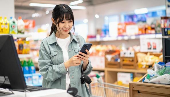 スーパーでスマホ決済を使う若い日本人女性 スーパーでスマホ決済を使う若い日本人女性の写真