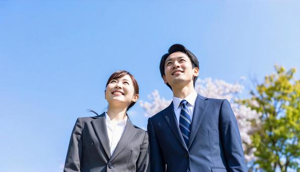 青空の下、遠くを見つめる若いスーツの男女 青空の下、遠くを見つめる若いスーツの男女の写真