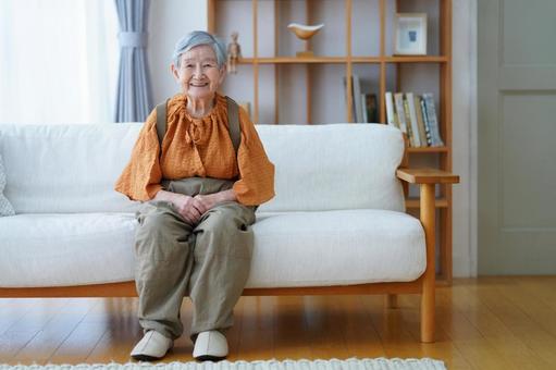 カメラ目線でソファに座る高齢女性 女性,笑顔,座るの写真素材