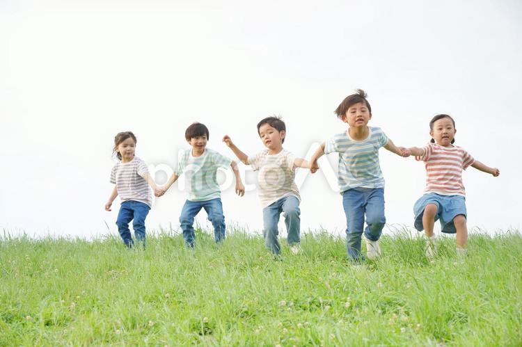 手を繋いで土手を駆け降りる小学生5人 男の子,女の子,女児の写真素材