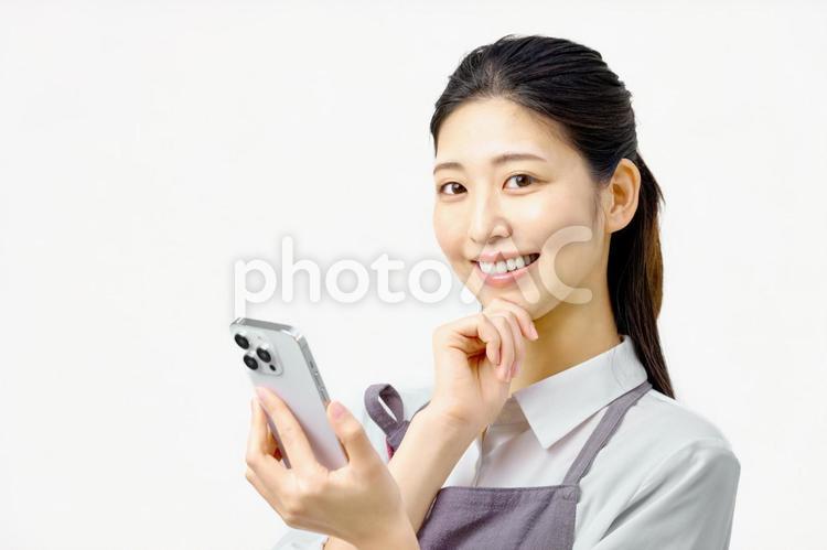 スマホを持ち考えるエプロンの女性　主婦 スマホ,女性,スマートフォンの写真素材