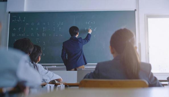 黒板に字を書く先生と授業を聞く生徒たち 黒板に字を書く先生と授業を聞く生徒たちの写真