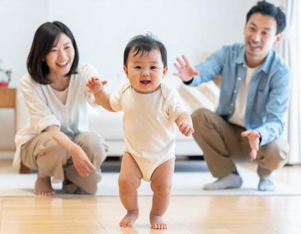 初めて歩いた赤ちゃんと見守る若い両親 初めて歩いた赤ちゃんと見守る若い両親の写真