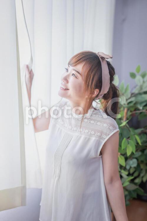 カーテンから差し込む朝日を浴びる若い女性 窓,朝日,換気の写真素材