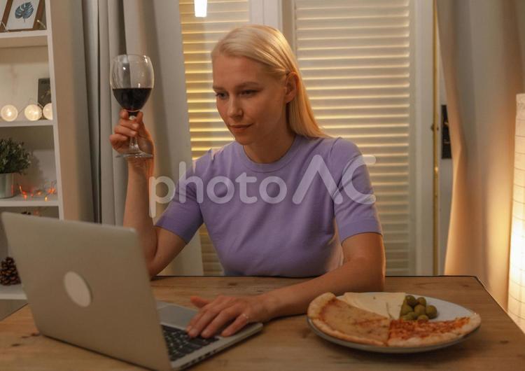 ワインを飲みながら真剣な顔でパソコンを見ている女性 女性,ワイン,パソコンの写真素材