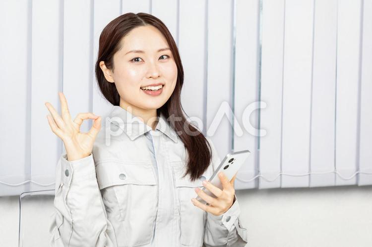 スマホを持ちOKサインの女性作業員01 作業員,女性,作業着の写真素材