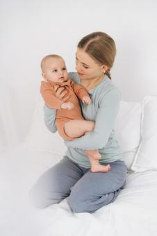 ベッドに正座して抱く赤ちゃんを見つめる女性 親子,母子,赤ちゃんの写真素材