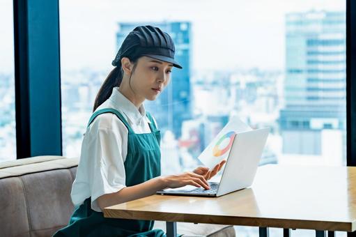パソコン作業をするエプロンをつけた女性 カフェ,スタッフ,店員の写真素材