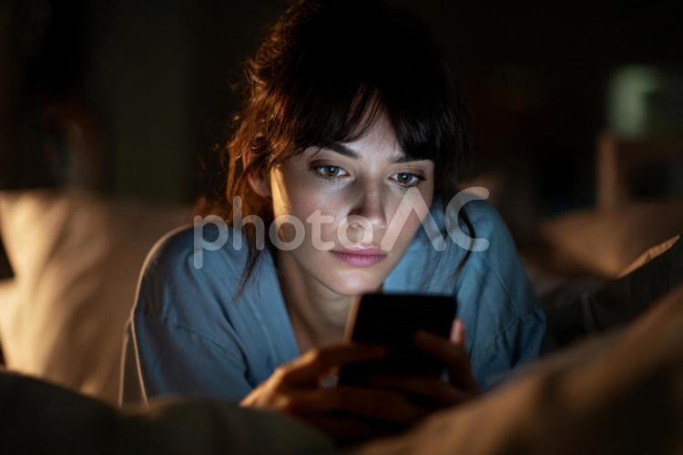 デジタル疲労：寝る前にスマホをする女性 女性,ベッド,夜の写真素材