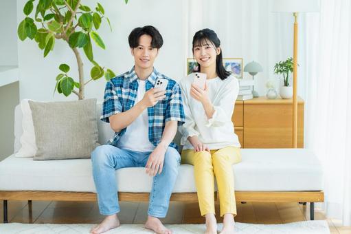 リビングでスマホを見るカップル リビングでスマホを見るカップル スマホ,笑顔,カップルの写真素材
