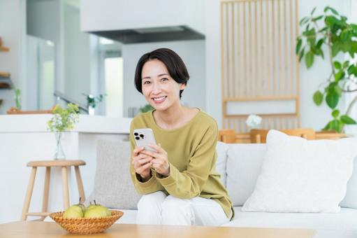 リビングでスマホを使うミドルの女性 リビングでスマホを使うミドルの女性の写真