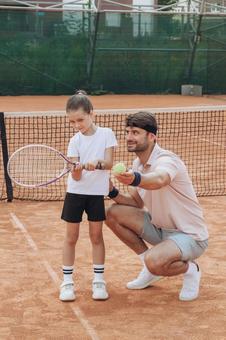 しゃがんでボールを示す男性とラケットを持つ女の子 親子,女の子,男性の写真素材