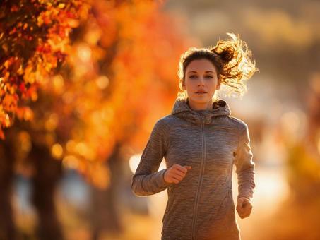 紅葉とジョギングする女性の写真