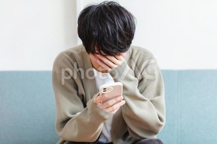 スマホを見て頭を抱える男性　 男性,悩み,泣くの写真素材