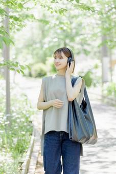 新緑の中ヘッドフォンで音楽を聴く若い女性 新緑の中ヘッドフォンで音楽を聴く若い女性 女性,外出,ヘッドフォンの写真素材