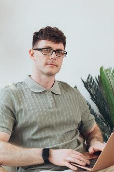 椅子に座って膝の上でノートパソコンを使うカメラ目線の男性 男性,外国人,欧米人の写真素材