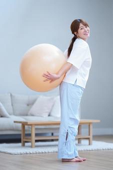 後ろでバランスボールを持ちカメラ目線の女性 女性,バランスボール,持つの写真素材