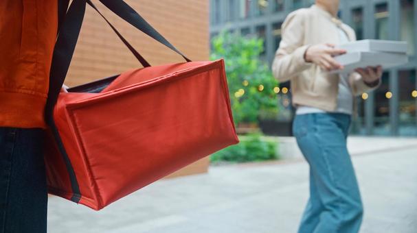 屋外でピザのデリバリーを受け取って帰る女性と配達員の男性 配達,フードデリバリー,デリバリーの写真素材