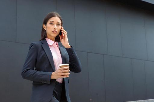オフィスビルの外でコーヒー片手に電話する外国人ビジネスウーマン ビジネスウーマン,ビジネス,女性の写真素材