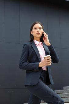オフィスビルの外の階段でコーヒー片手に電話しているアジア人ビジネスウーマン ビジネスウーマン,ビジネス,女性の写真素材