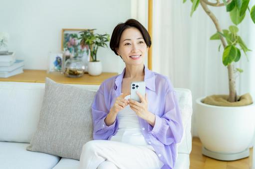 部屋でスマホを使うミドル女性 スマホ,笑顔,女性の写真素材