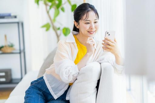 部屋でスマホを操作する女性 スマホ,笑顔,部屋の写真素材