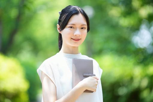 公園で女性が本を片手に持ちカメラ目線 女性,本,手帳の写真素材