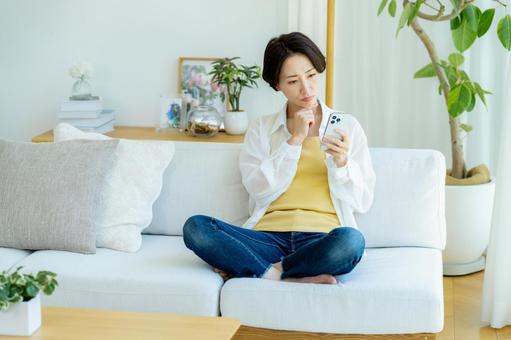 部屋でスマホを使うミドル女性 部屋でスマホを使うミドル女性 スマホ,悩む,困るの写真素材