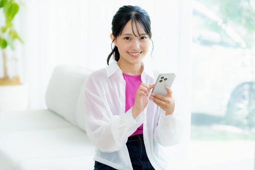 部屋でスマホを操作する若い女性 スマホ,若い女性,笑顔の写真素材