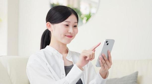 リビングでスマホを操作するアジア人女性 スマートフォン,操作,女性の写真素材