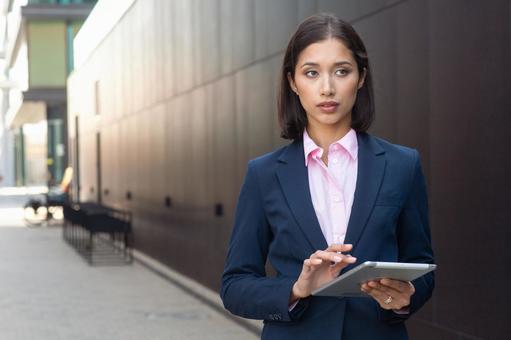 街なかでタブレットを使っているスーツのアジア人女性 ビジネスウーマン,ビジネス,女性の写真素材