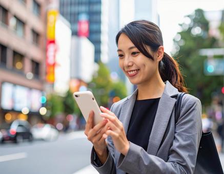 オフィス街でスマホを操作する女性社員 オフィス街でスマホを操作する女性社員の写真