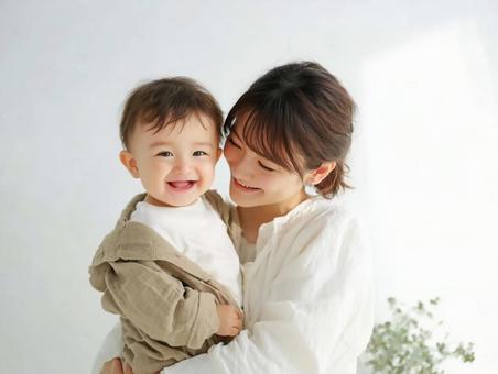室内で母親に抱かれて笑顔を見せる赤ちゃん 室内で母親に抱かれて笑顔を見せる赤ちゃんの写真
