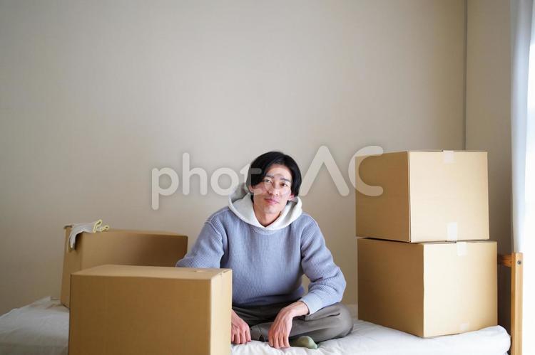 引っ越し中にベッドであぐらをかいている男性 引っ越し,一人暮らし,男性の写真素材