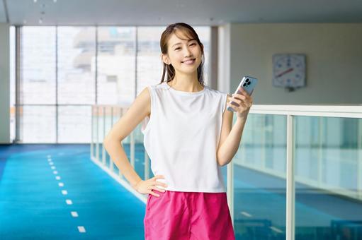 ジムでスマホを見る笑顔の女性 スポーツジム,スマホ,女性の写真素材
