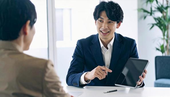 タブレットを使って説明する男性営業マンの写真