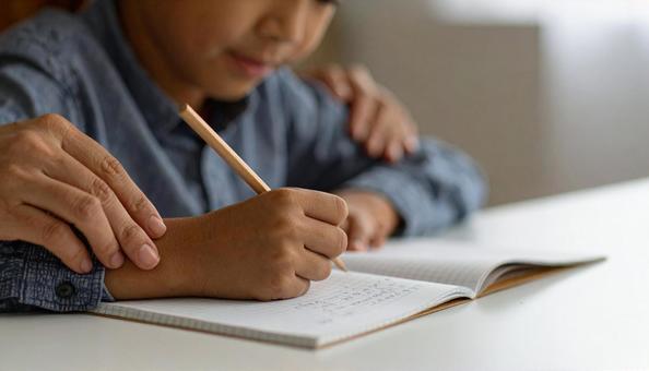 宿題に取り組む男の子の手と寄り添う母親 宿題に取り組む男の子の手と寄り添う母親の写真