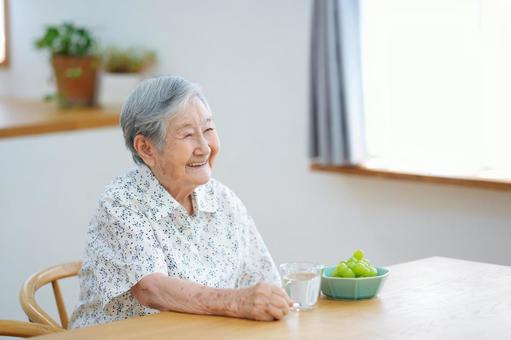 窓際の席に座り笑う高齢女性 女性,笑顔,シャインマスカットの写真素材