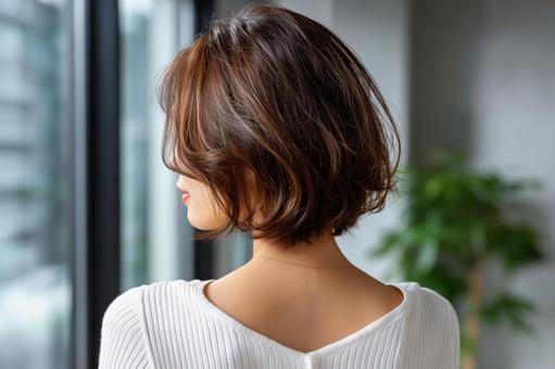 窓辺に立つボブヘアの若い女性の後ろ姿の写真