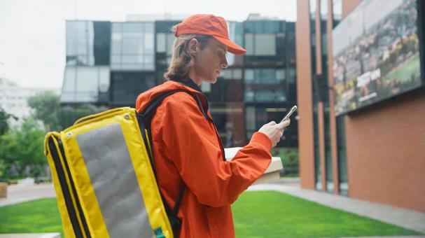 街なかでスマートフォンを見ている横向きのフードデリバリーの男性の写真