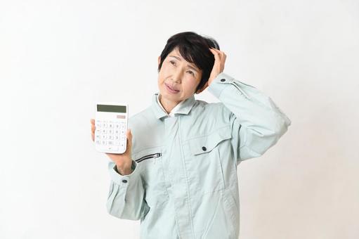 電卓を持ちながら困る作業服姿の中高年女性 作業員,女性,ミドル女性の写真素材