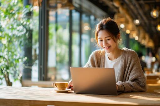 カフェでノートパソコン操作する笑顔の女性 カフェでノートパソコン操作する笑顔の女性の写真