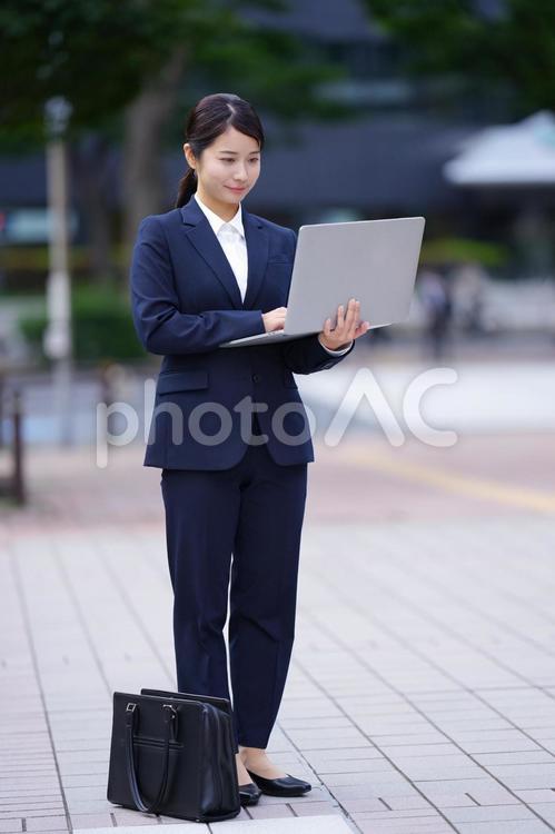 バッグを下に置いてパソコンを見て立っている女性 女性,人物,大学生の写真素材