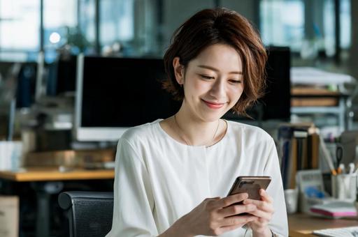 オフィスでスマホを見る女性-2 オフィスでスマホを見る女性-2の写真